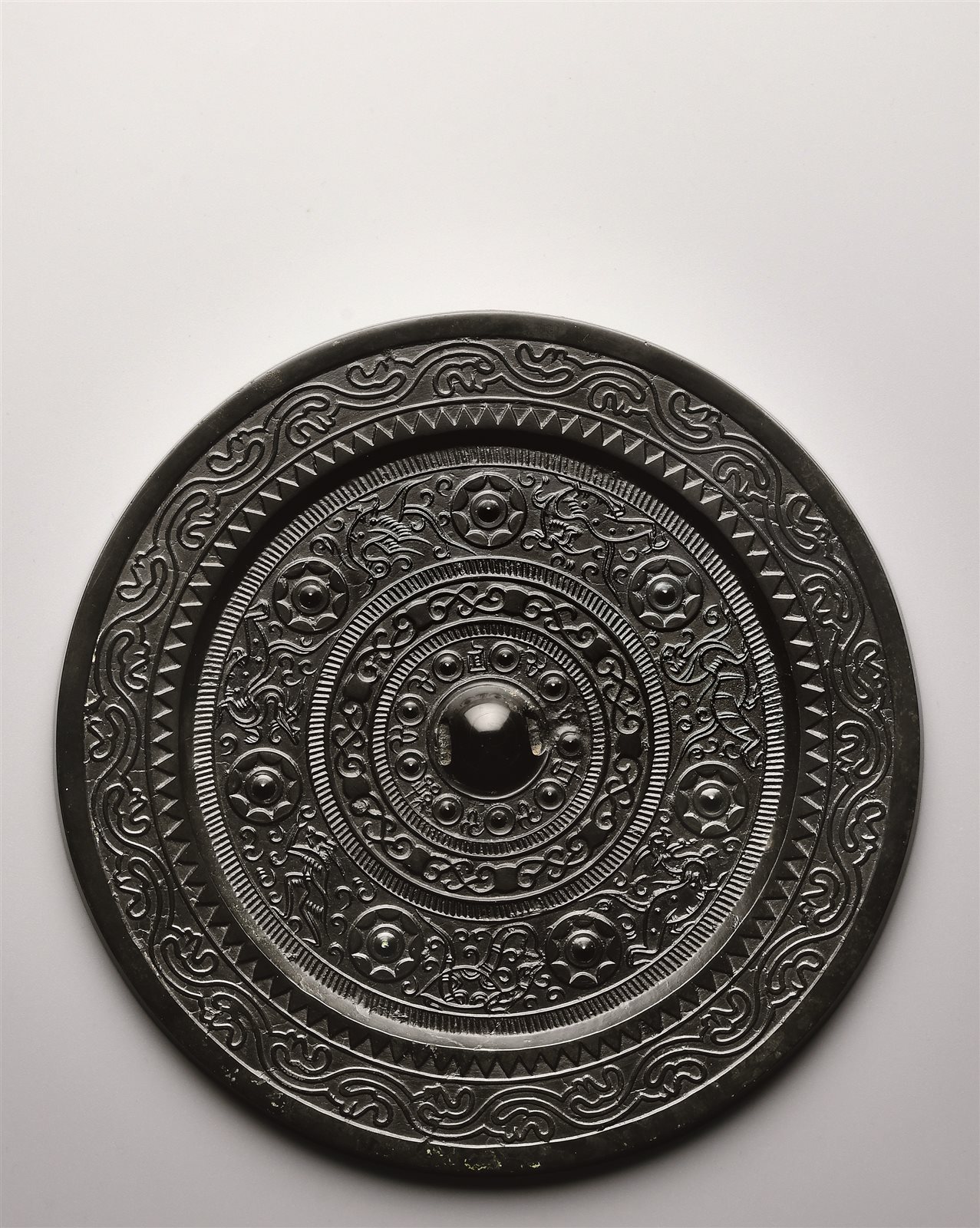 其外两圈栉齿纹之间饰图案化的缠枝花草纹,外面两圈栉齿纹之间的主题